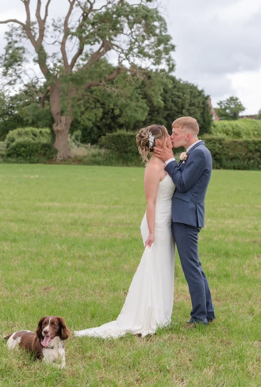 Bride and groom kissing in a countryside field with their dog in the foreground